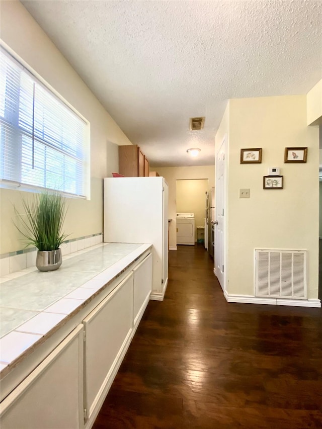 hall featuring washer / dryer, dark wood-style floors, a textured ceiling, and visible vents