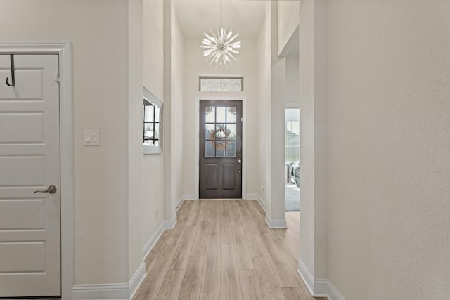 doorway to outside featuring baseboards, a chandelier, and light wood-type flooring
