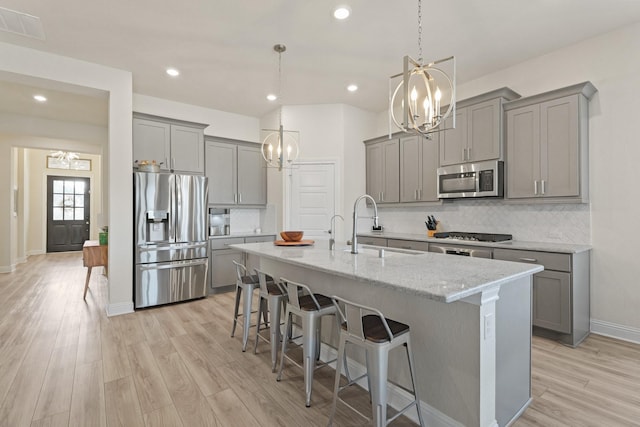 kitchen with gray cabinets, a kitchen island with sink, stainless steel appliances, and a chandelier