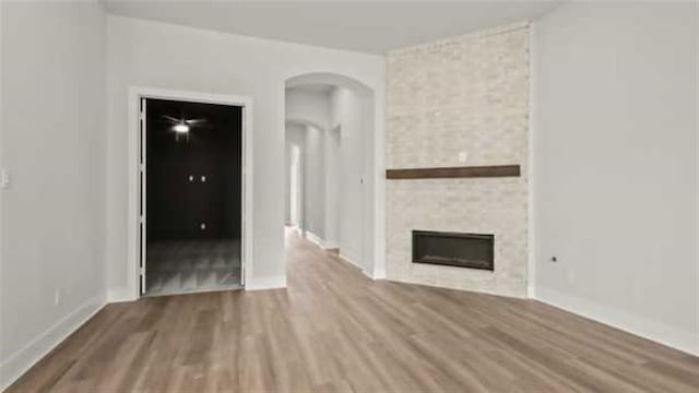 15615 Broadway Bnd, Conroe, TX 77302 - unfurnished living room featuring baseboards, arched walkways, wood finished floors, and a stone fireplace