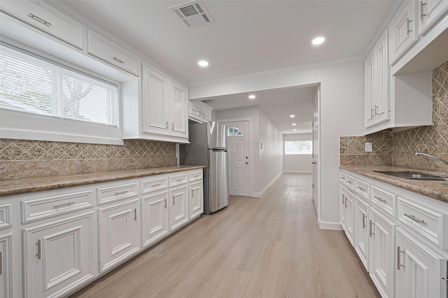 kitchen with freestanding refrigerator, white cabinetry, visible vents, a sink, and baseboards