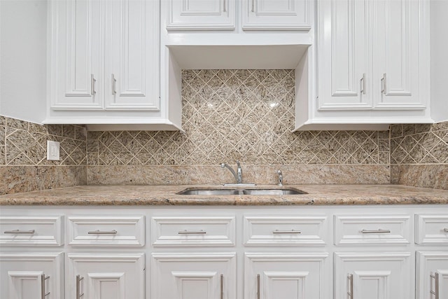 kitchen with a sink, white cabinets, decorative backsplash, and light stone countertops