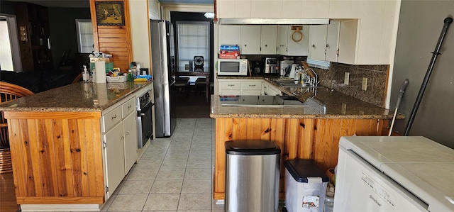kitchen with tasteful backsplash, oven, a peninsula, white microwave, and light tile patterned flooring
