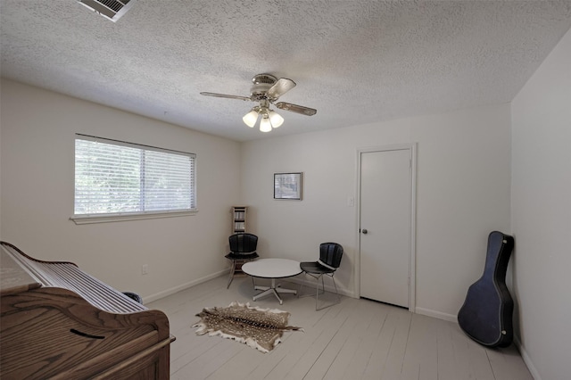 sitting room with visible vents, baseboards, a ceiling fan, light wood-type flooring, and a textured ceiling