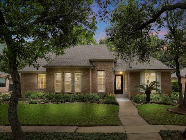 view of front facade featuring a shingled roof, brick siding, and a yard