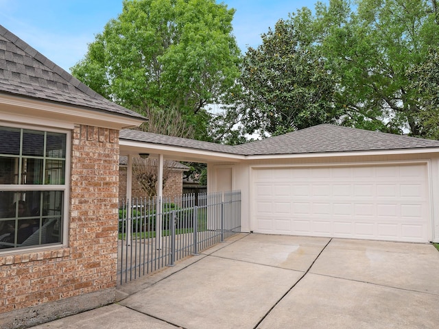 exterior space with concrete driveway, an attached garage, fence, brick siding, and roof with shingles