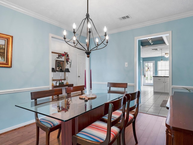 dining area with wood finished floors, visible vents, crown molding, and a notable chandelier
