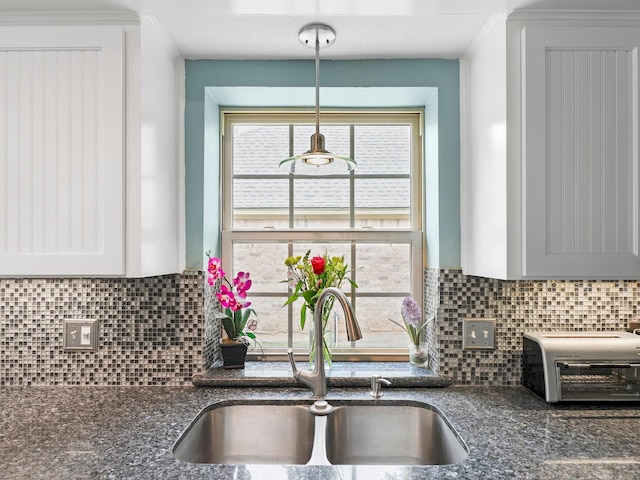 kitchen featuring a toaster, backsplash, dark stone counters, and a sink