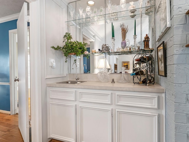 bar with light wood-style flooring, crown molding, and a sink