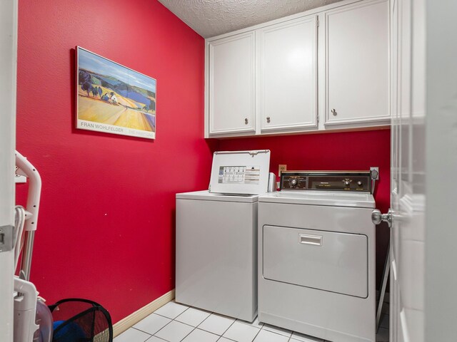 washroom featuring washer and clothes dryer, a textured ceiling, light tile patterned flooring, cabinet space, and baseboards