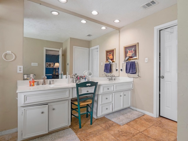 bathroom with a textured ceiling, double vanity, visible vents, and a sink