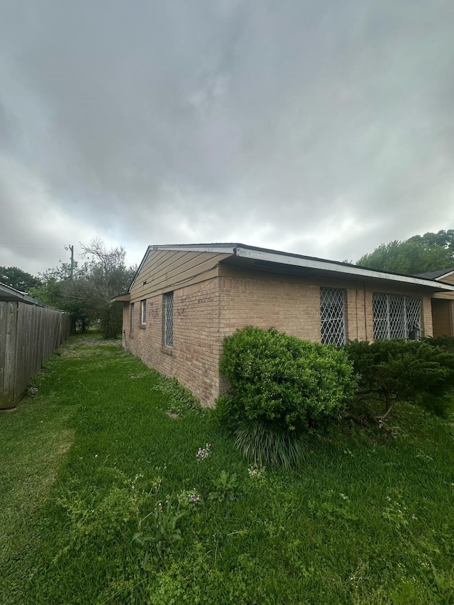 view of home's exterior with a yard, brick siding, and fence