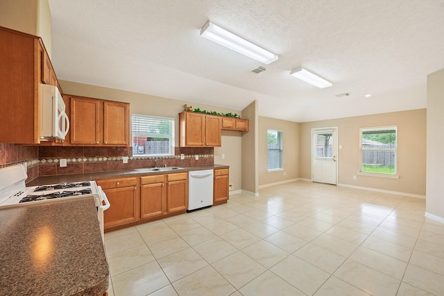 kitchen with lofted ceiling, backsplash, dark countertops, a sink, and white appliances