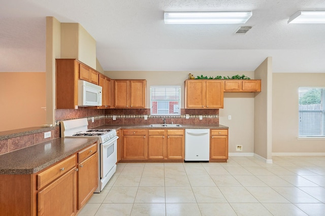 kitchen with dark countertops, visible vents, a sink, white appliances, and tasteful backsplash