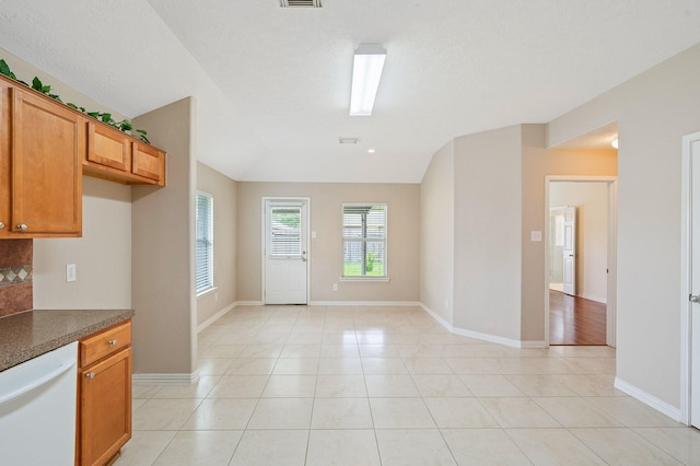 kitchen featuring light tile patterned flooring, dark countertops, baseboards, white dishwasher, and brown cabinets