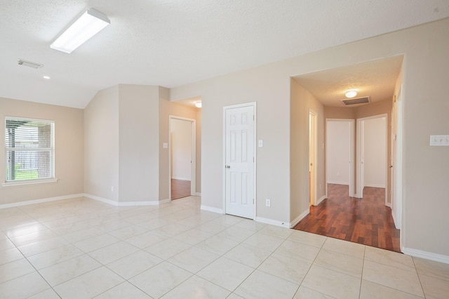 empty room featuring visible vents, a textured ceiling, and light tile patterned flooring