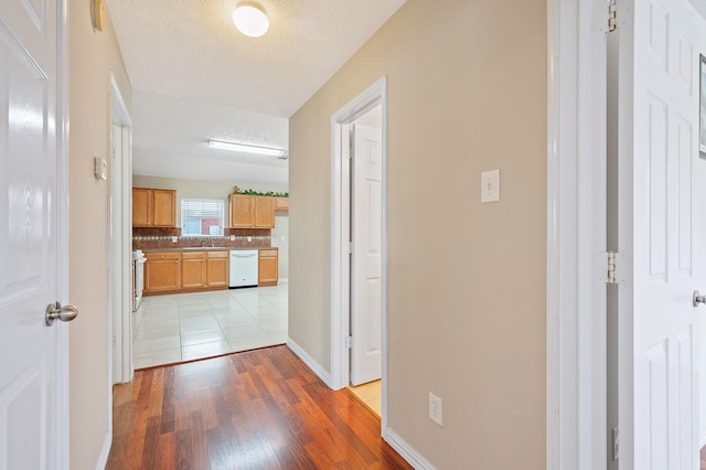 corridor with baseboards, a sink, and light wood-style floors