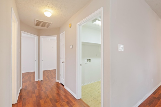 corridor featuring a textured ceiling, wood finished floors, visible vents, and baseboards