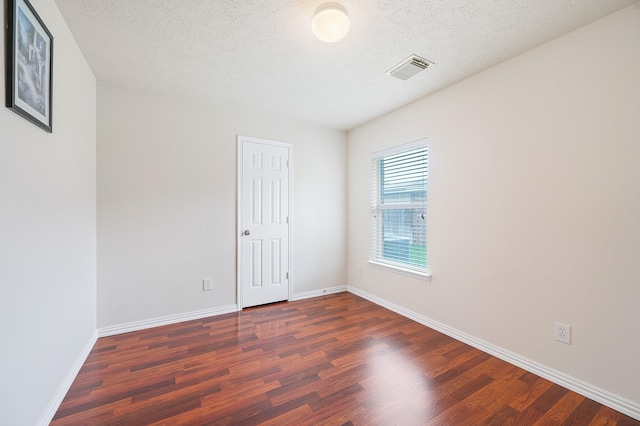 empty room with dark wood-type flooring, a textured ceiling, visible vents, and baseboards