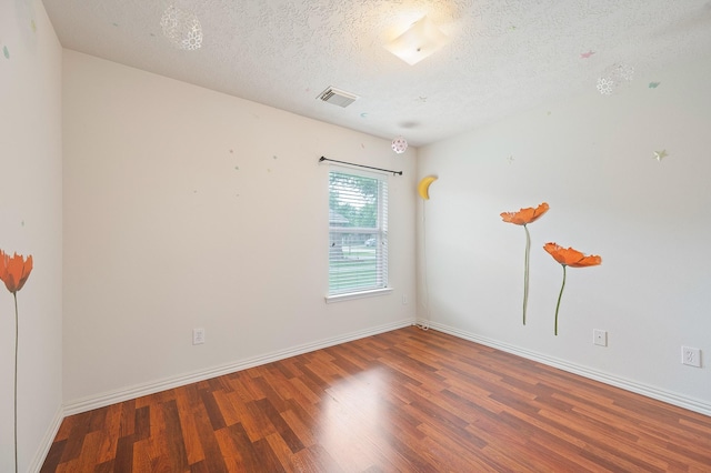 unfurnished room with wood finished floors, a textured ceiling, baseboards, and visible vents