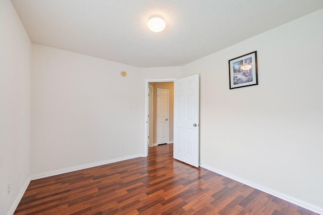 unfurnished room featuring baseboards and dark wood-type flooring