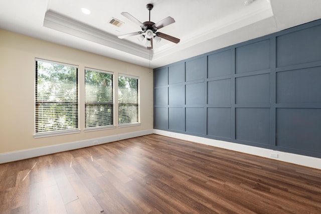 empty room with crown molding, a tray ceiling, ceiling fan, a decorative wall, and wood finished floors