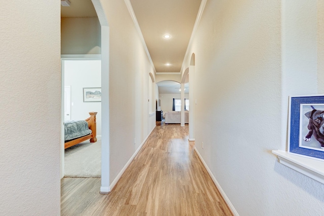 hallway featuring crown molding, arched walkways, baseboards, and light wood-style floors