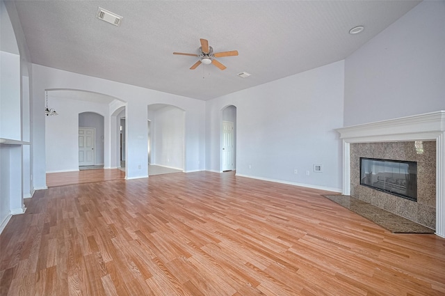 19915 Hardsville Dr, Spring, TX 77388 - unfurnished living room featuring ceiling fan, light wood-style flooring, a tile fireplace, baseboards, and arched walkways