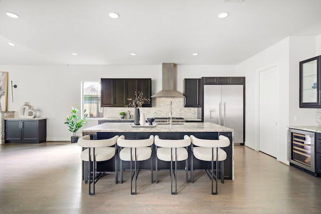 kitchen with wall chimney range hood, a kitchen breakfast bar, built in fridge, and wine cooler