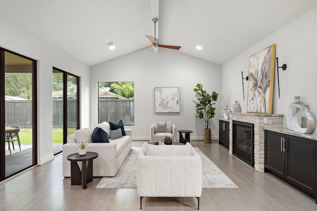 living area featuring light wood-style floors, a ceiling fan, vaulted ceiling, and a fireplace