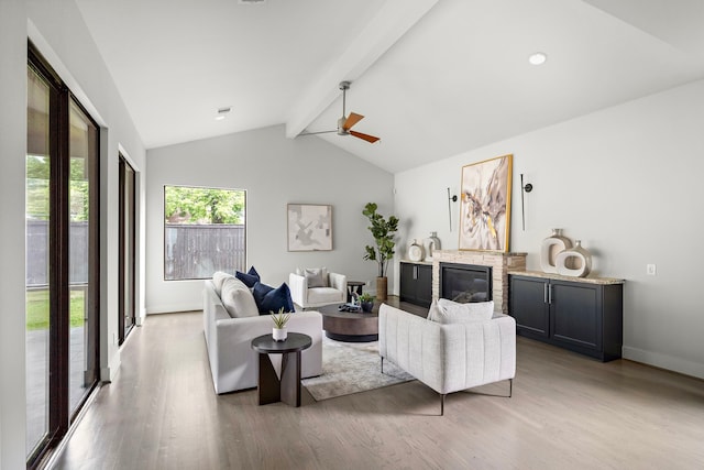 living room featuring baseboards, vaulted ceiling with beams, a fireplace, and wood finished floors