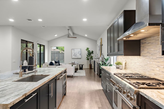 kitchen featuring wall chimney exhaust hood, lofted ceiling with beams, light wood finished floors, backsplash, and stainless steel appliances