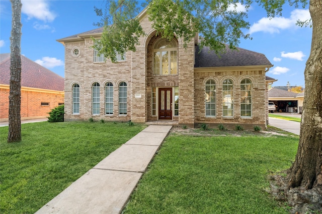 view of front of house featuring roof with shingles, a front yard, brick siding, and french doors