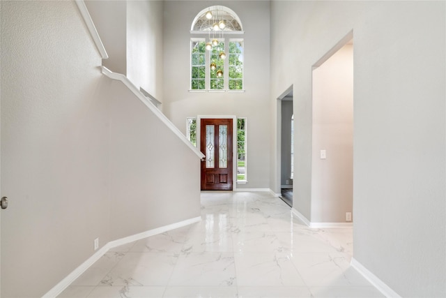 foyer entrance with marble finish floor, baseboards, a notable chandelier, and a towering ceiling