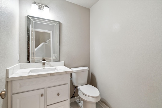 bathroom featuring toilet, vanity, a textured wall, and walk in shower