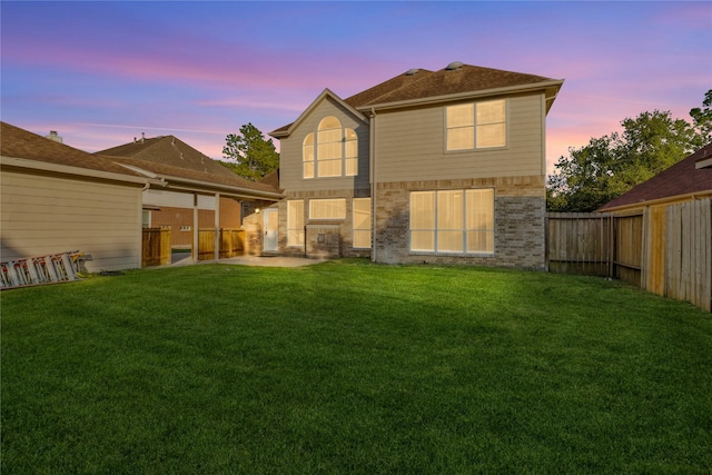 back of house at dusk with a yard, a fenced backyard, brick siding, and a patio area