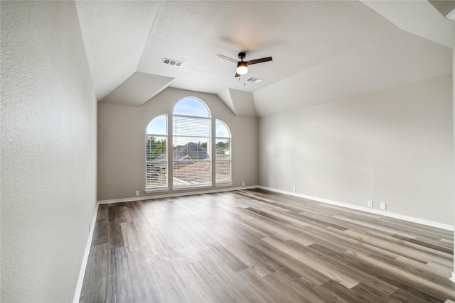 unfurnished room featuring a ceiling fan, vaulted ceiling, visible vents, wood finished floors, and baseboards