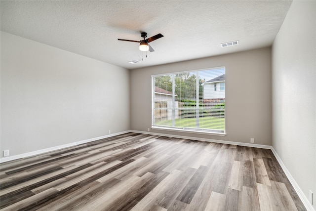 empty room with a textured ceiling, a ceiling fan, visible vents, wood finished floors, and baseboards
