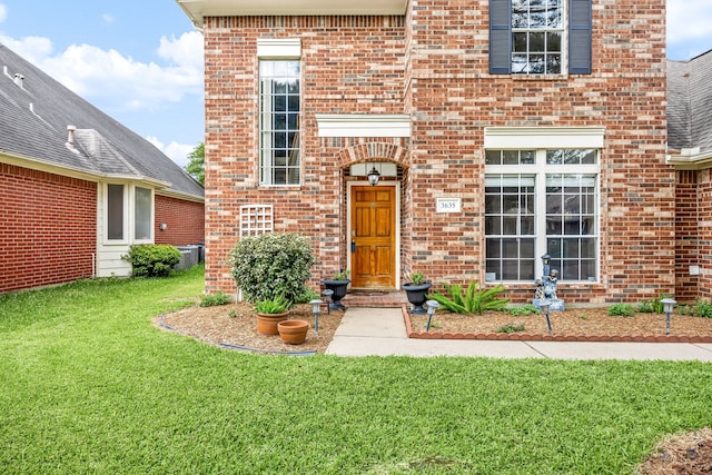 view of exterior entry featuring a lawn and brick siding
