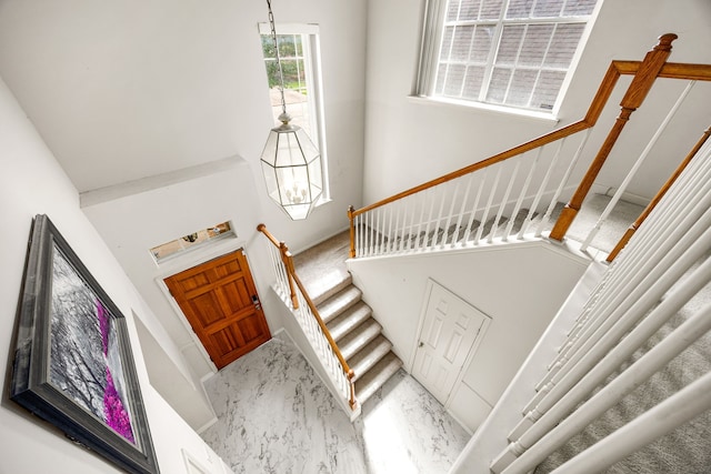 entryway featuring stairway, marble finish floor, a notable chandelier, and a towering ceiling