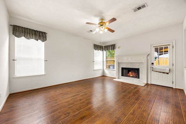 unfurnished living room with ceiling fan, dark wood-type flooring, visible vents, and a tiled fireplace