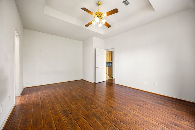 empty room with hardwood / wood-style flooring, ceiling fan, a raised ceiling, baseboards, and visible vents