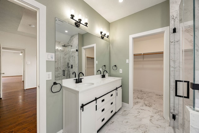 bathroom with double vanity, a spacious closet, a marble finish shower, and a sink