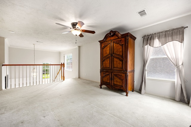 spare room featuring a ceiling fan, light carpet, baseboards, ornamental molding, and visible vents