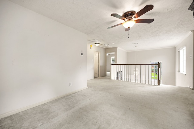 empty room with crown molding, a textured ceiling, attic access, ceiling fan, and carpet