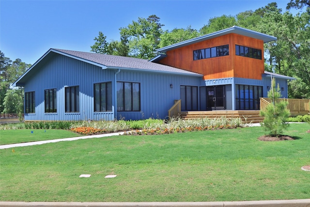 back of property with a shingled roof and a lawn