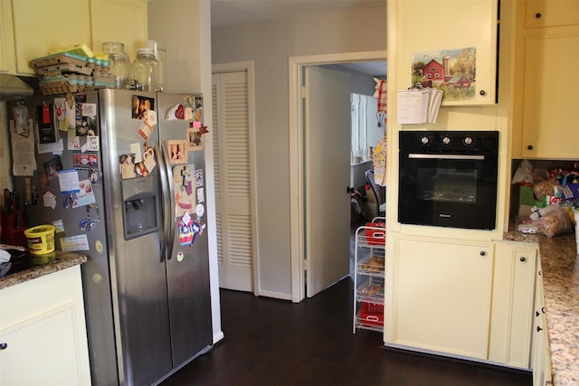 kitchen featuring light stone countertops, oven, dark wood-style flooring, and stainless steel fridge with ice dispenser