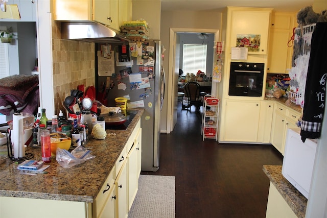 kitchen featuring oven, stone counters, under cabinet range hood, dark wood-type flooring, and freestanding refrigerator