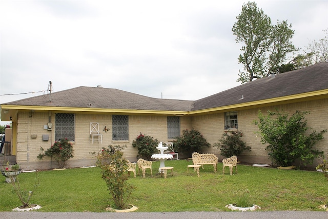 view of front of house with brick siding, roof with shingles, and a front yard