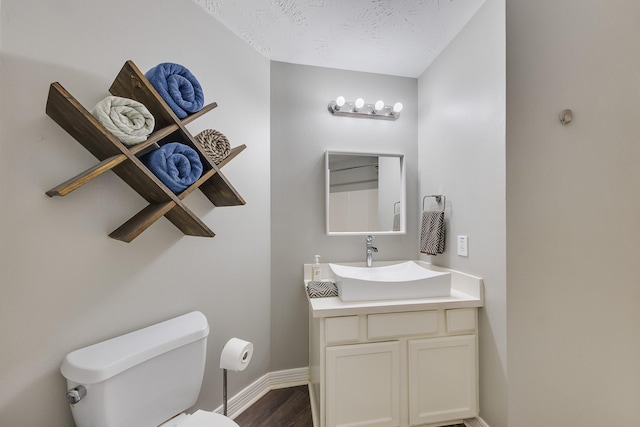half bath with toilet, wood finished floors, vanity, and baseboards